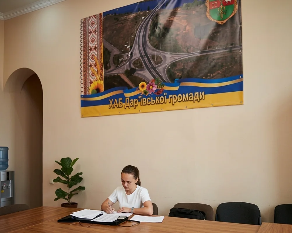 Жінка заповнює документи за столом під банером хабу Дар’ївської громади