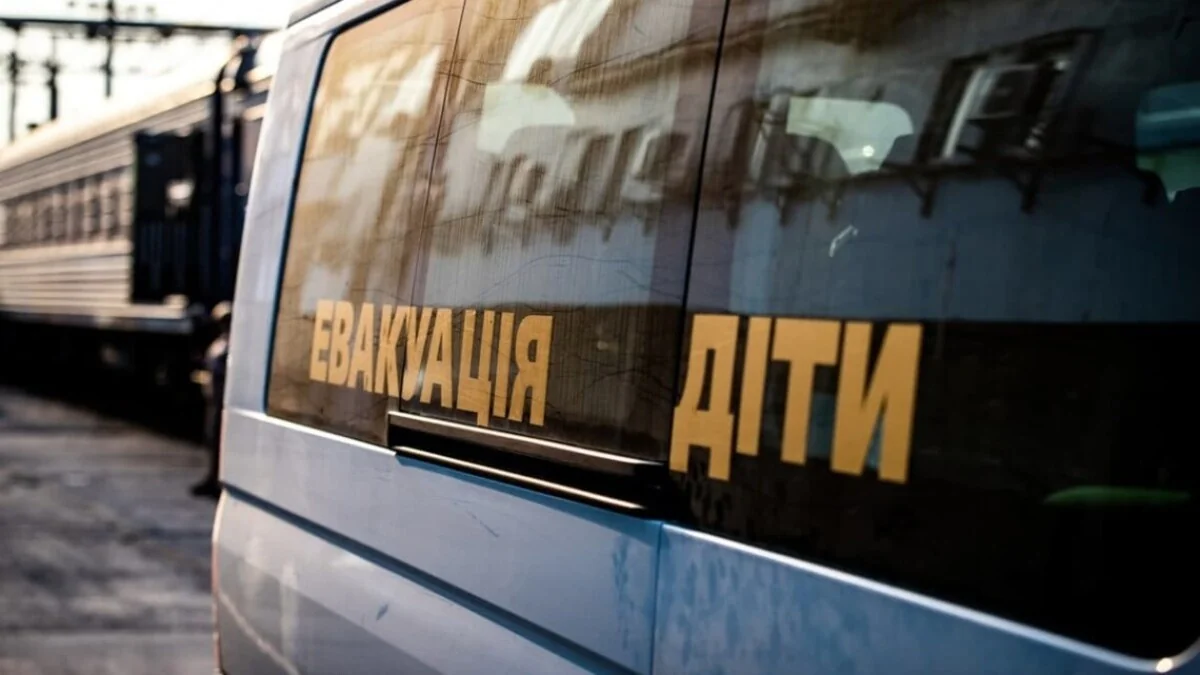 Білий мікроавтобус з жовтими написами Евакуація і Діти біля поїзда