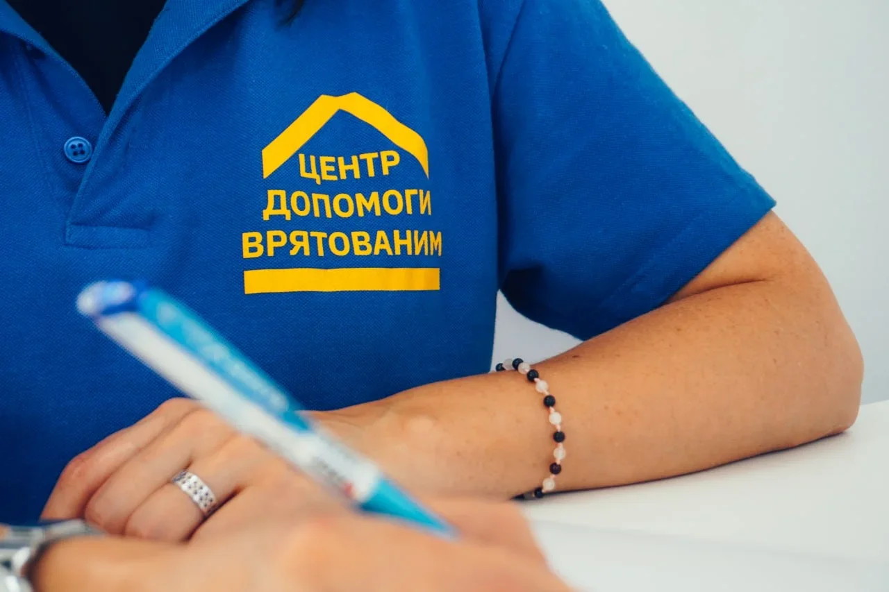 Працівниця в синьому поло Центру допомоги врятованим пише ручкою