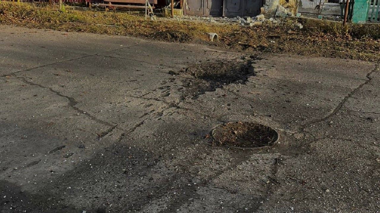 Потрісканий асфальт з люком і вибоїною біля будинків на вулиці