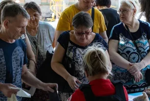 Люди біля столу з працівницею в червоній жилетці розглядають документи на відкритому майданчику