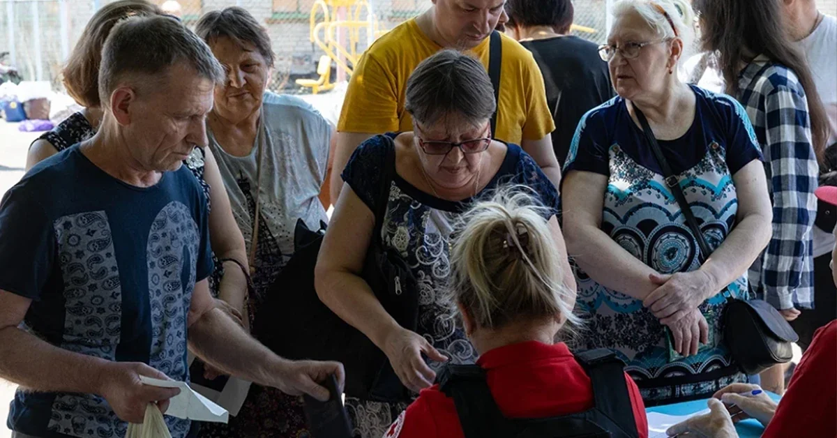 Люди біля столу з працівницею в червоній жилетці розглядають документи на відкритому майданчику