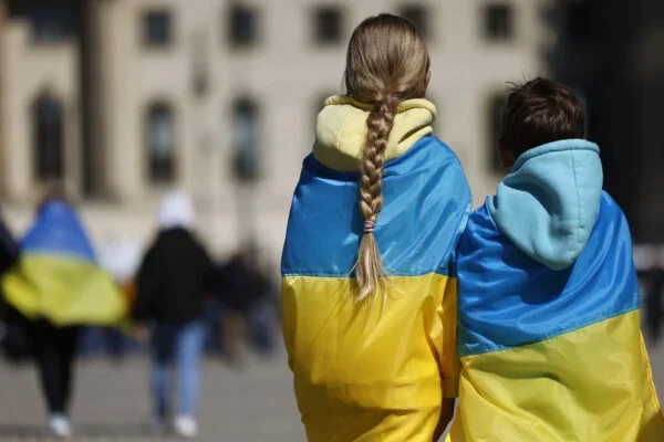 Двоє дітей стоять спинами, загорнуті в українські прапори на площі